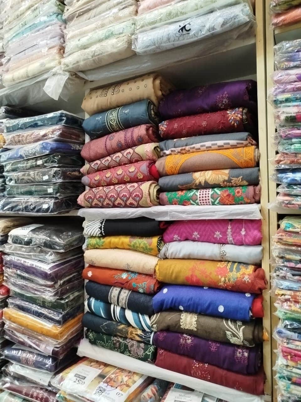 Embroidered ladies suits folded on the shelves at Shahzad Cloth House