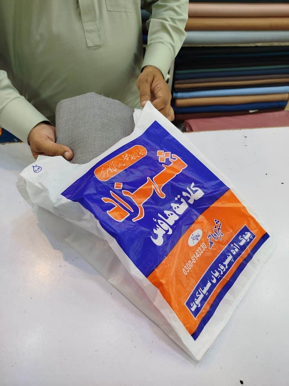 Putting fabric into a Shahzad Cloth House bag with the shop name in Urdu