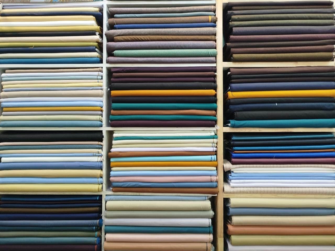 Shelves of plain suiting in white, grey, navy, black and khaki at Shahzad Cloth House